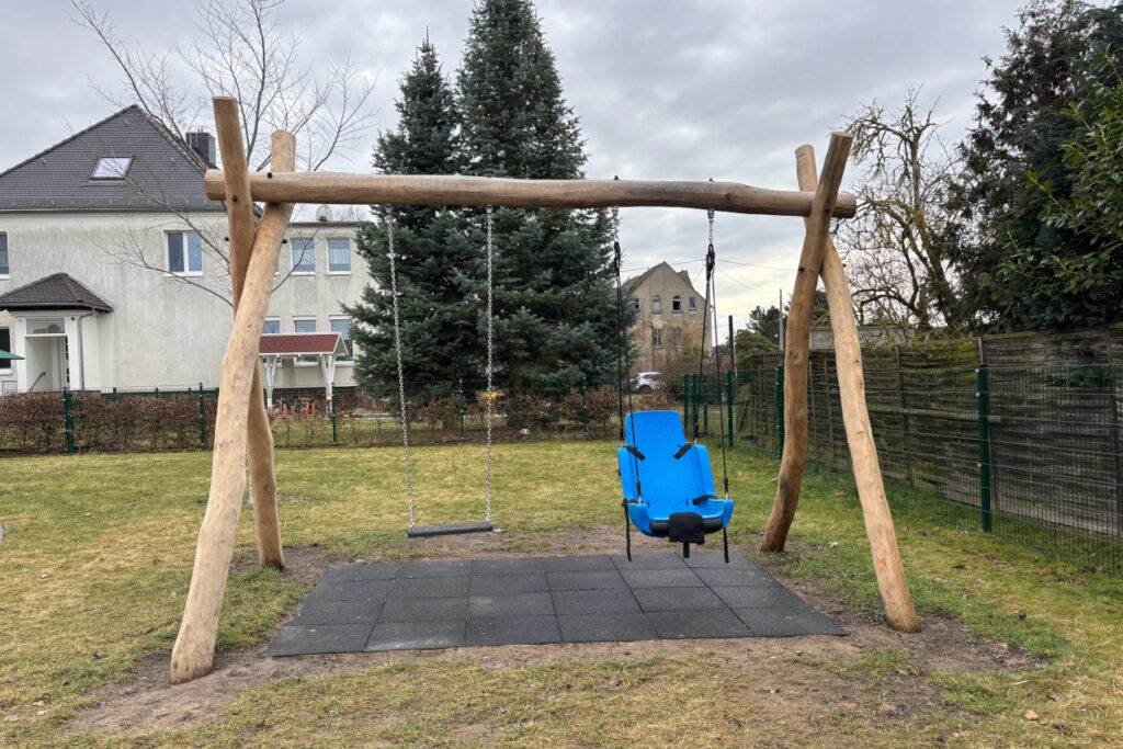 Eine Doppelschaukel mit einem Sitzbrett und einem Kindersitz mit Lehne und Anschnallmöglichkeiten