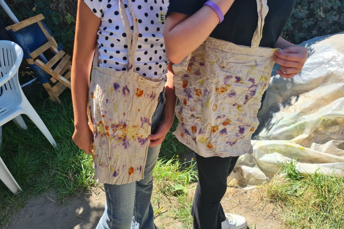 Zwei Jugendliche stehen auf einer Wiese und haben selbstbedruckte Jutebeutel umgehängt. Die Gesichter sind nicht zu sehen.